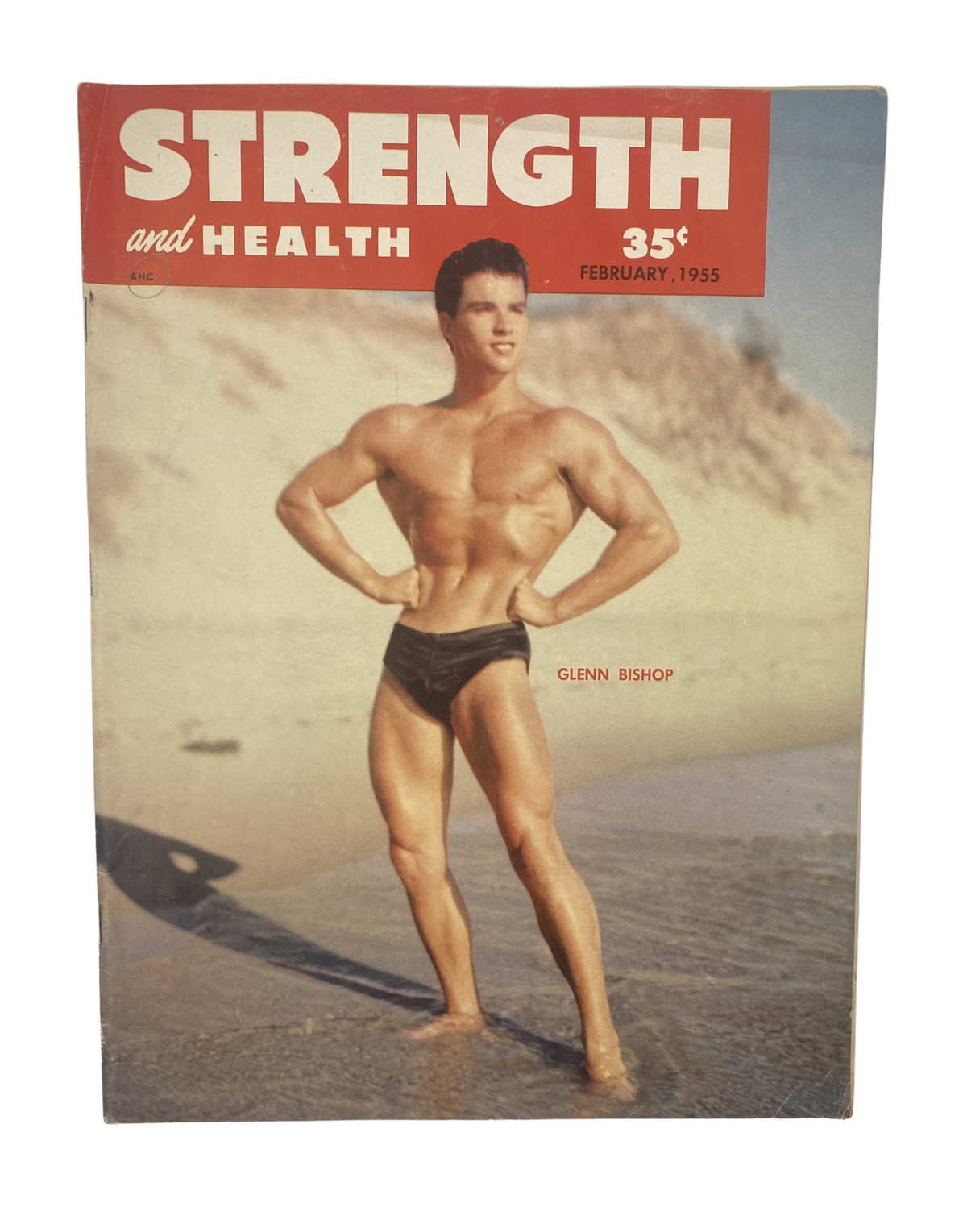 Cover of Strength and Health Magazine February 1955 featuring Glenn Bishop showcasing a muscular physique on the beach, highlighting weightlifting culture.