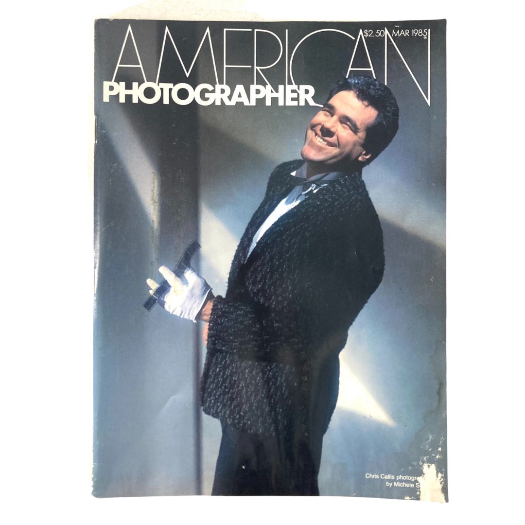 Cover of American Photographer Magazine March 1985 featuring Chris Callis, photographed by Michele Singer, showcasing a smiling man in a stylish black attire.